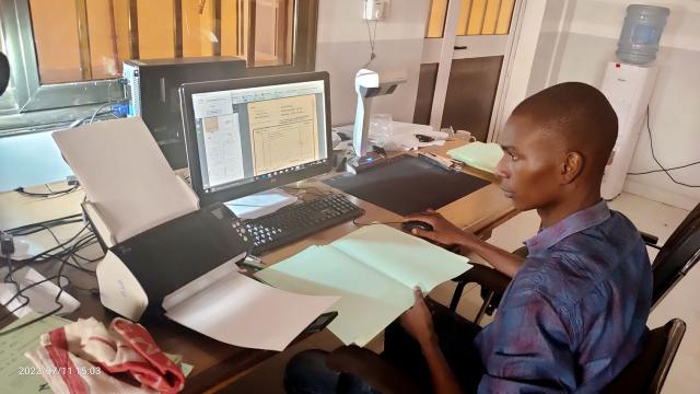 Jeune homme burkinabè assis derrière un bureau en train de scanner des documents