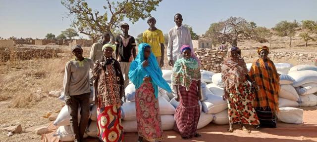 Ten beneficiaries from the commune of Sangha stand in front of a delivery of millet sacks
