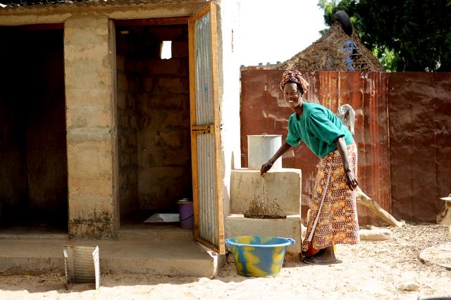 Une femme en tenue colorée lave des vêtements. Elle remplit une bassine d’eau au robinet