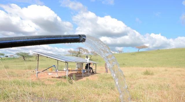 Panneau solaire dans un champ, avec au premier plan un tuyau d'où jaillit de l'eau