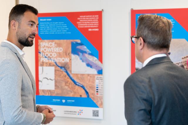 2 persons talking in front of an exhibition panel